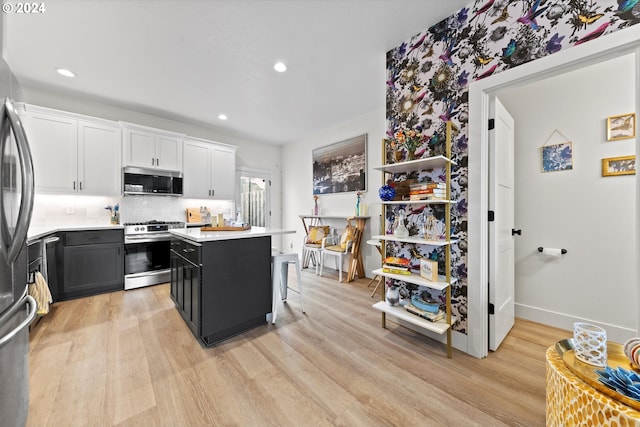 kitchen with tasteful backsplash, light wood-type flooring, stainless steel appliances, white cabinets, and a kitchen bar