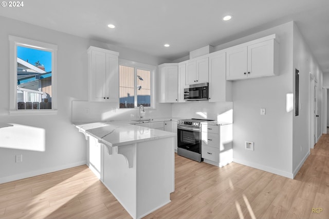 kitchen with kitchen peninsula, a breakfast bar, white cabinetry, sink, and stainless steel appliances