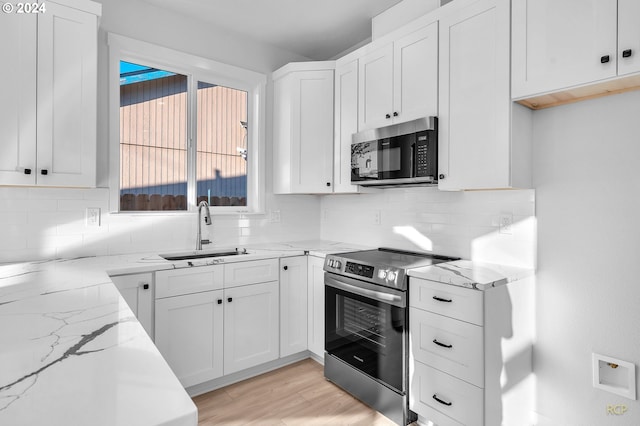 kitchen featuring sink, white cabinetry, stainless steel appliances, light stone counters, and light hardwood / wood-style flooring