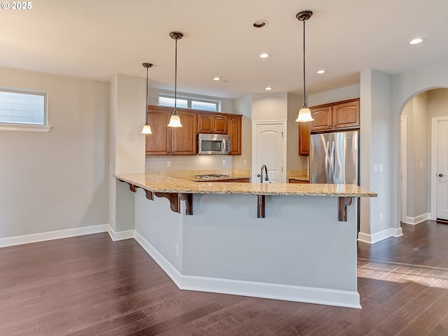 kitchen featuring a kitchen bar, decorative light fixtures, kitchen peninsula, stainless steel appliances, and light stone countertops