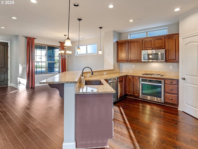 kitchen with pendant lighting, sink, light stone counters, kitchen peninsula, and stainless steel appliances