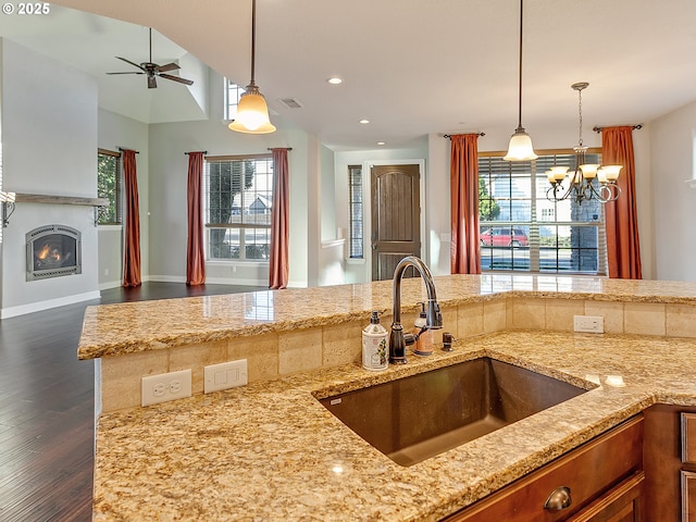 kitchen featuring pendant lighting, sink, dark wood-type flooring, ceiling fan, and light stone counters