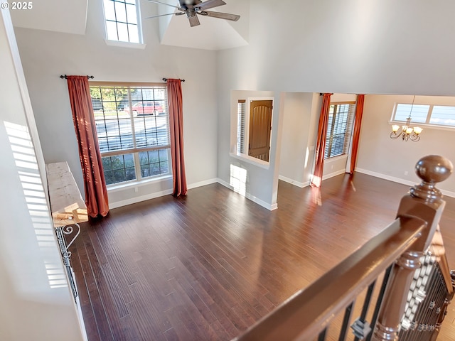 interior space featuring ceiling fan with notable chandelier, dark wood-type flooring, a healthy amount of sunlight, and a towering ceiling