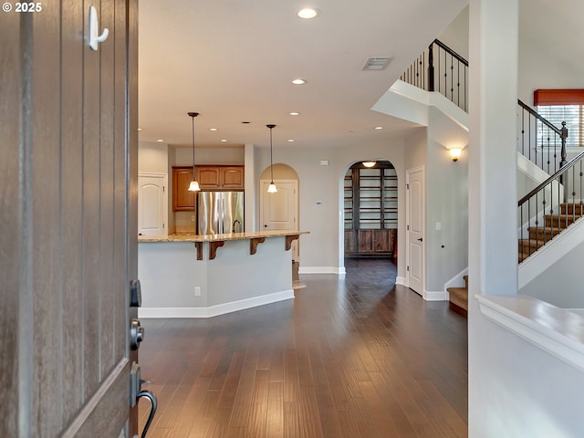 interior space featuring dark wood-type flooring, a breakfast bar area, light stone counters, decorative light fixtures, and stainless steel fridge