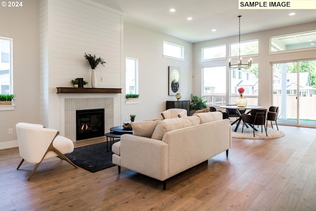 living room with light wood-type flooring, a fireplace, a high ceiling, and an inviting chandelier