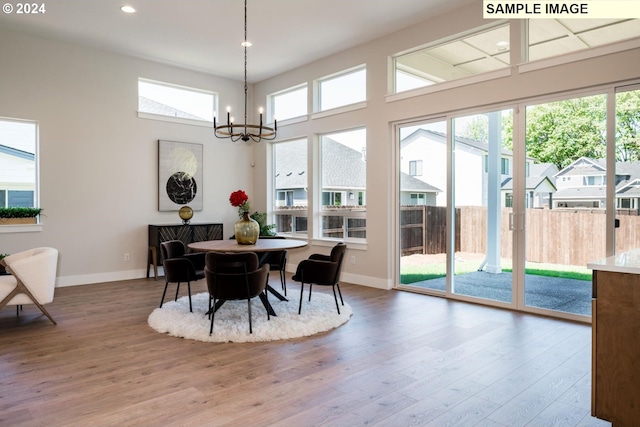 dining space with a notable chandelier, a healthy amount of sunlight, wood-type flooring, and a high ceiling