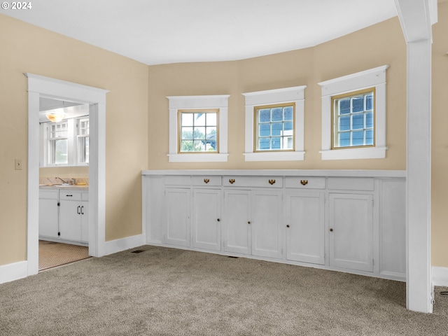 bar with sink, light carpet, and white cabinetry