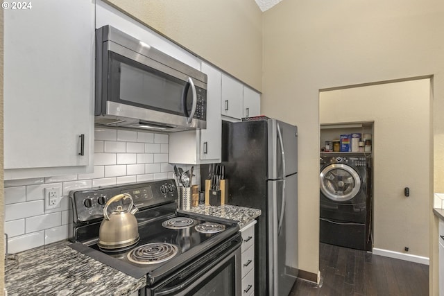 kitchen with dark wood-type flooring, dark stone countertops, stainless steel appliances, washer / clothes dryer, and white cabinets