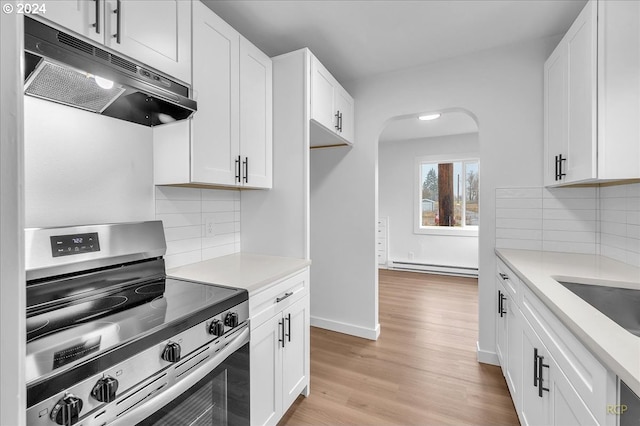 kitchen with decorative backsplash, white cabinetry, stainless steel stove, and light hardwood / wood-style flooring