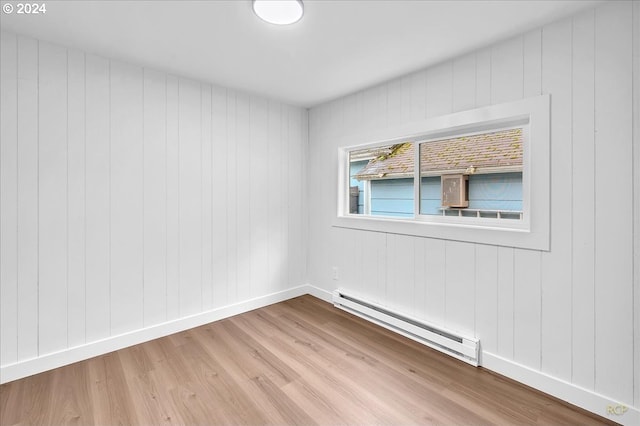 unfurnished room featuring wooden walls, light hardwood / wood-style flooring, and a baseboard heating unit