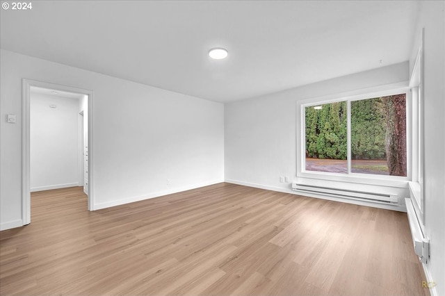 spare room featuring baseboard heating and light hardwood / wood-style floors