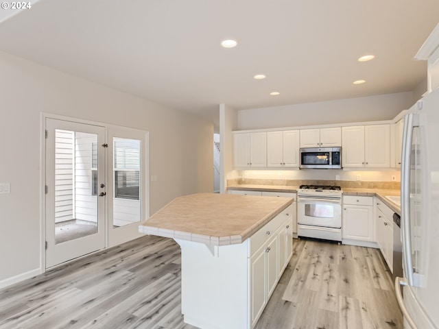 kitchen with a kitchen bar, white cabinetry, a center island, light wood-type flooring, and white appliances