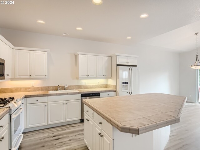 kitchen with appliances with stainless steel finishes, white cabinets, pendant lighting, and light hardwood / wood-style floors