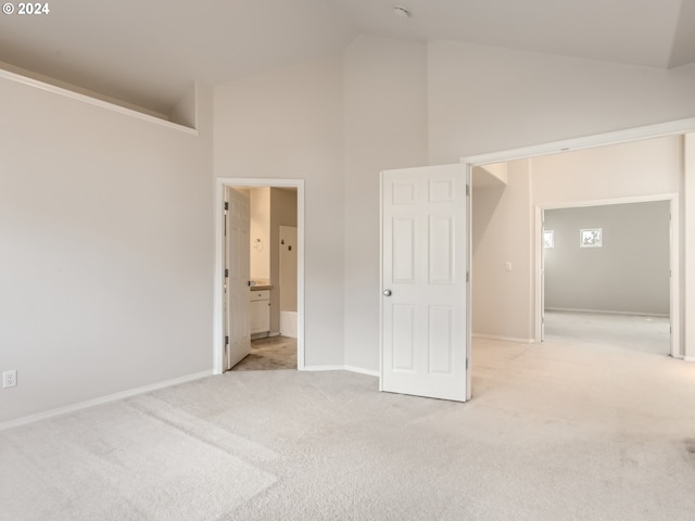 unfurnished bedroom featuring connected bathroom, high vaulted ceiling, and light carpet