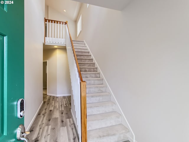 stairs with hardwood / wood-style flooring and high vaulted ceiling