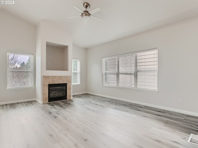 unfurnished living room featuring ceiling fan, a tiled fireplace, a healthy amount of sunlight, and light hardwood / wood-style floors