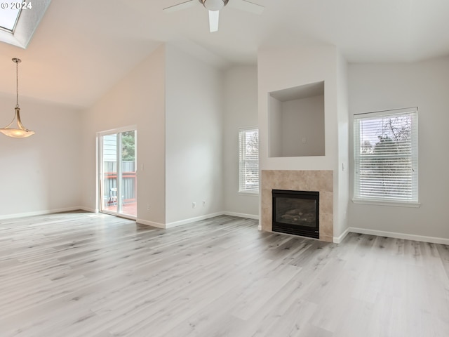 unfurnished living room with light hardwood / wood-style flooring, ceiling fan, high vaulted ceiling, a skylight, and a tile fireplace