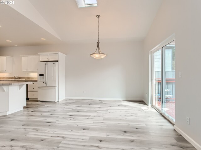 unfurnished dining area featuring vaulted ceiling with skylight, sink, and light hardwood / wood-style flooring