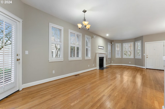 unfurnished living room with a notable chandelier, a healthy amount of sunlight, and light hardwood / wood-style floors