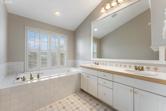 bathroom featuring vanity, a relaxing tiled tub, and vaulted ceiling