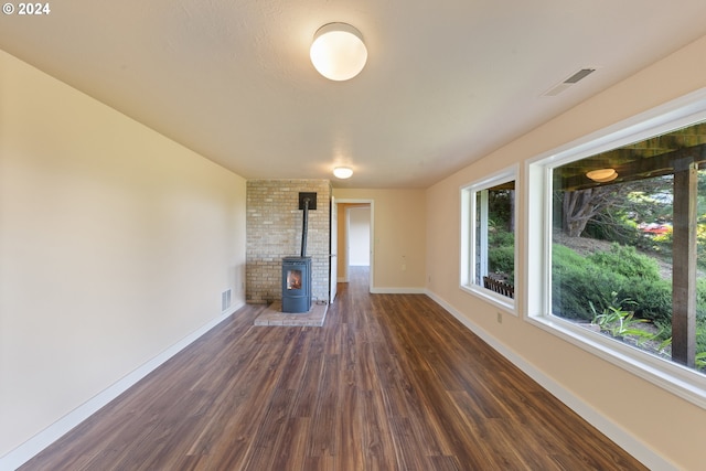 unfurnished living room featuring brick wall, dark wood-type flooring, and a wood stove