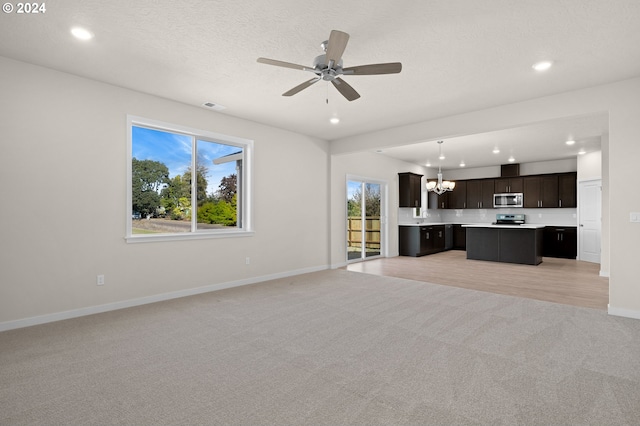 unfurnished living room with light carpet, a textured ceiling, and ceiling fan with notable chandelier