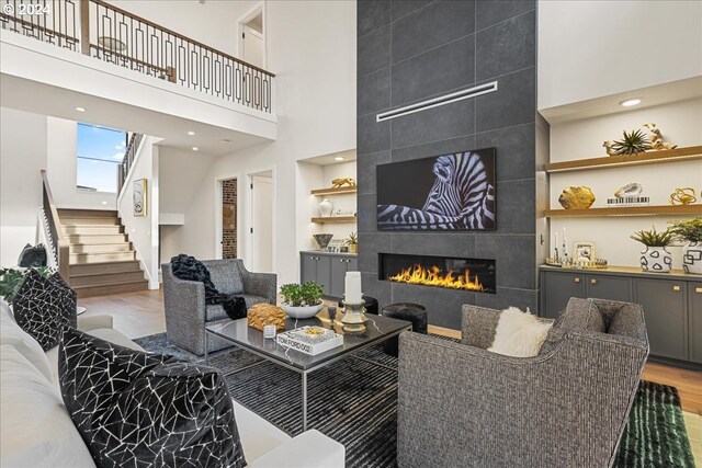 living room with a tile fireplace, a high ceiling, built in features, and hardwood / wood-style flooring