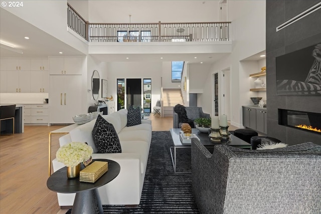 living room with light wood-type flooring, a tiled fireplace, and a towering ceiling