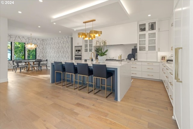 kitchen featuring white cabinets, decorative light fixtures, light wood-type flooring, and a kitchen island with sink