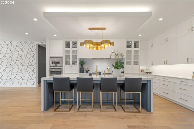 kitchen featuring a breakfast bar, light hardwood / wood-style floors, hanging light fixtures, and a large island with sink