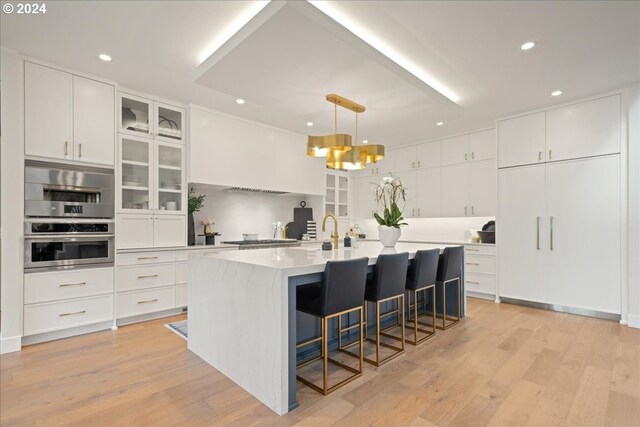 kitchen featuring light wood-type flooring, white cabinetry, and a kitchen island with sink