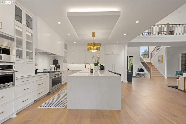 kitchen with an island with sink, decorative light fixtures, white cabinetry, appliances with stainless steel finishes, and light hardwood / wood-style floors