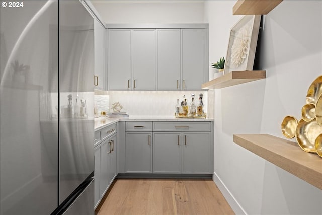 kitchen featuring stainless steel refrigerator, light wood-type flooring, tasteful backsplash, and gray cabinetry