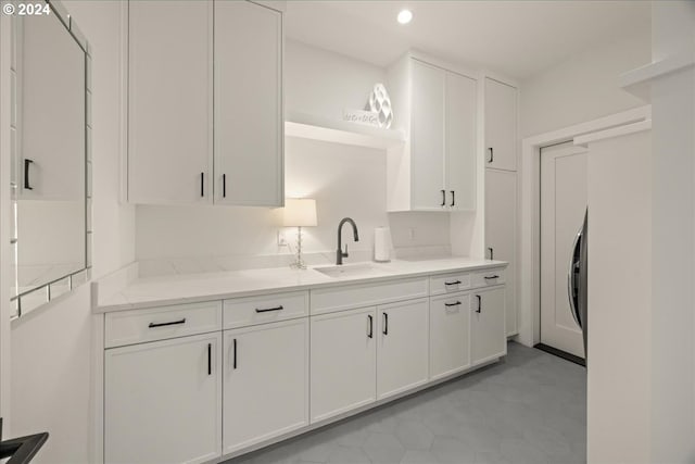 kitchen with washer / clothes dryer, white cabinetry, sink, and light stone counters