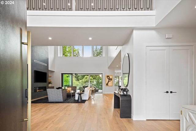 living room with light hardwood / wood-style floors, a towering ceiling, and a large fireplace