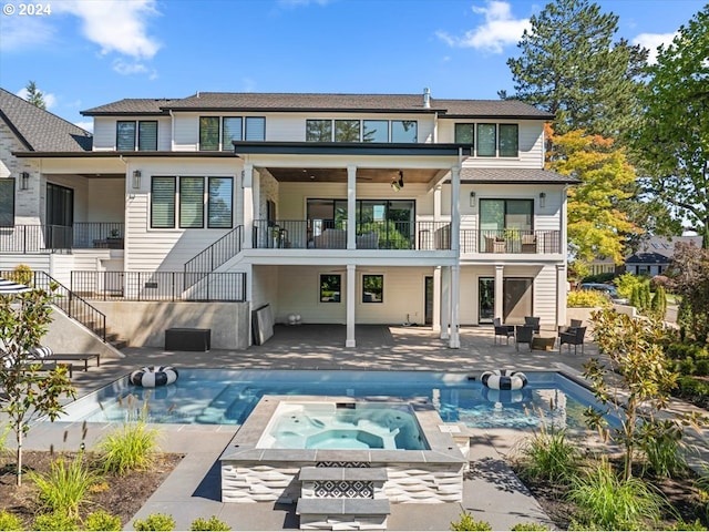 back of property with a balcony, ceiling fan, a swimming pool with hot tub, and a patio area