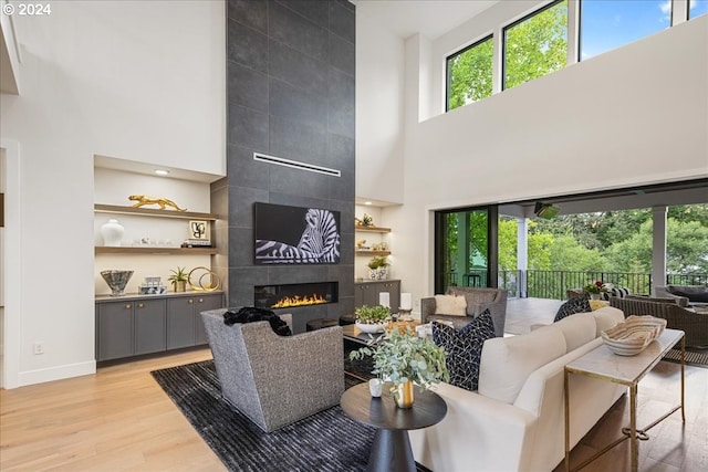 living room with built in shelves, light hardwood / wood-style flooring, a high ceiling, and a tile fireplace