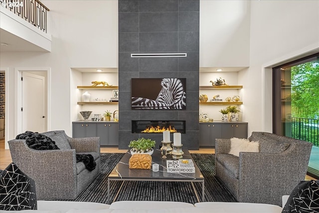 living room with wood-type flooring, a fireplace, a towering ceiling, and built in shelves