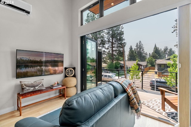 living room with a wall unit AC, light hardwood / wood-style flooring, and a towering ceiling