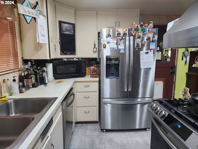 kitchen with appliances with stainless steel finishes, white cabinetry, sink, and range hood