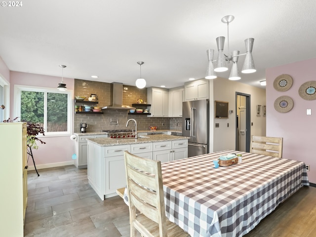 kitchen with high end refrigerator, white cabinets, pendant lighting, and wall chimney range hood