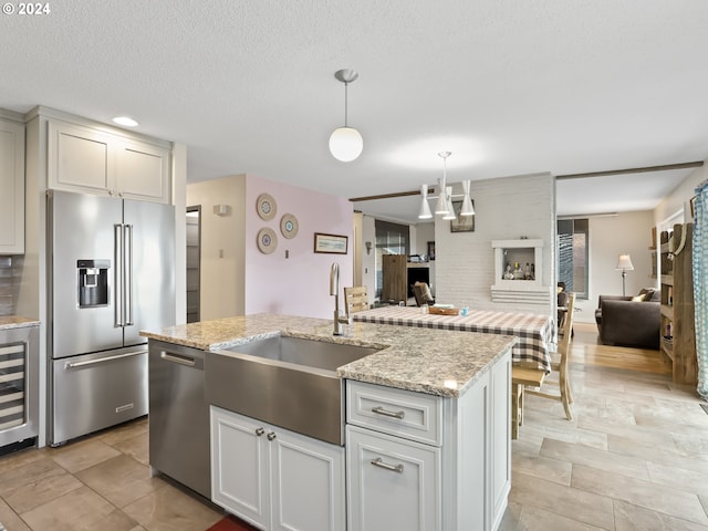 kitchen with light stone countertops, sink, hanging light fixtures, stainless steel appliances, and a kitchen island with sink