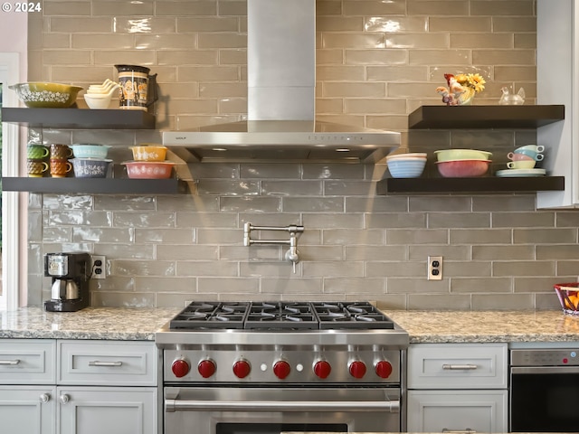 kitchen featuring backsplash, wall chimney exhaust hood, appliances with stainless steel finishes, light stone counters, and white cabinetry