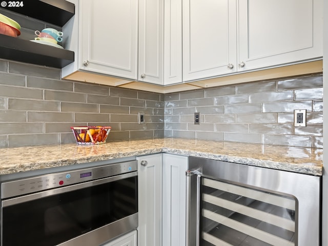 kitchen with white cabinets, wine cooler, light stone countertops, and stainless steel oven