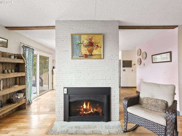 living room featuring beamed ceiling, light hardwood / wood-style floors, a stone fireplace, and a textured ceiling