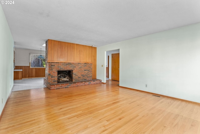 unfurnished living room featuring light wood-type flooring, a textured ceiling, a fireplace, and wooden walls