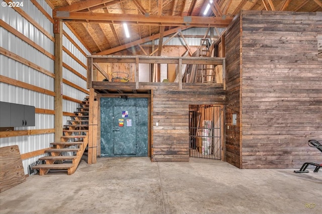 unfurnished living room with high vaulted ceiling, wooden walls, and concrete flooring