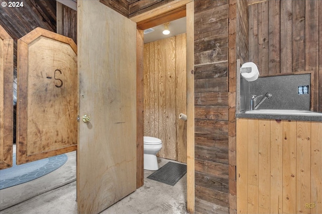 bathroom with concrete floors, wooden walls, and toilet