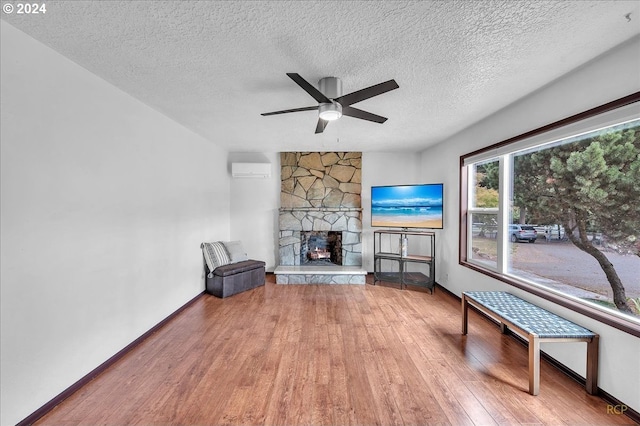 unfurnished room with ceiling fan, wood-type flooring, a stone fireplace, a textured ceiling, and a wall unit AC