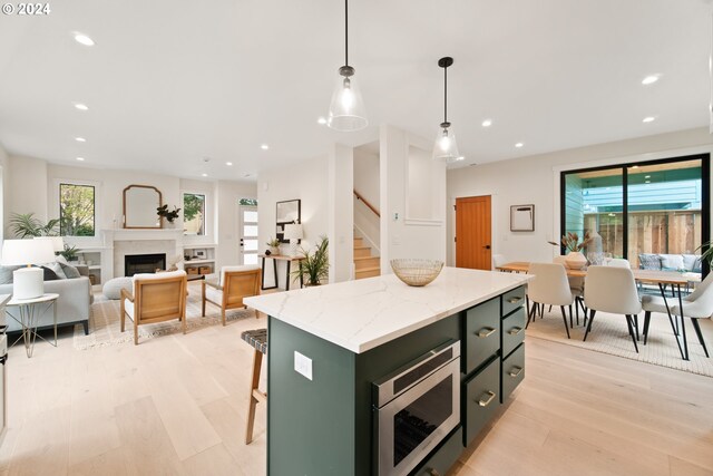 kitchen with hanging light fixtures, light stone counters, a kitchen island, stainless steel microwave, and light hardwood / wood-style flooring